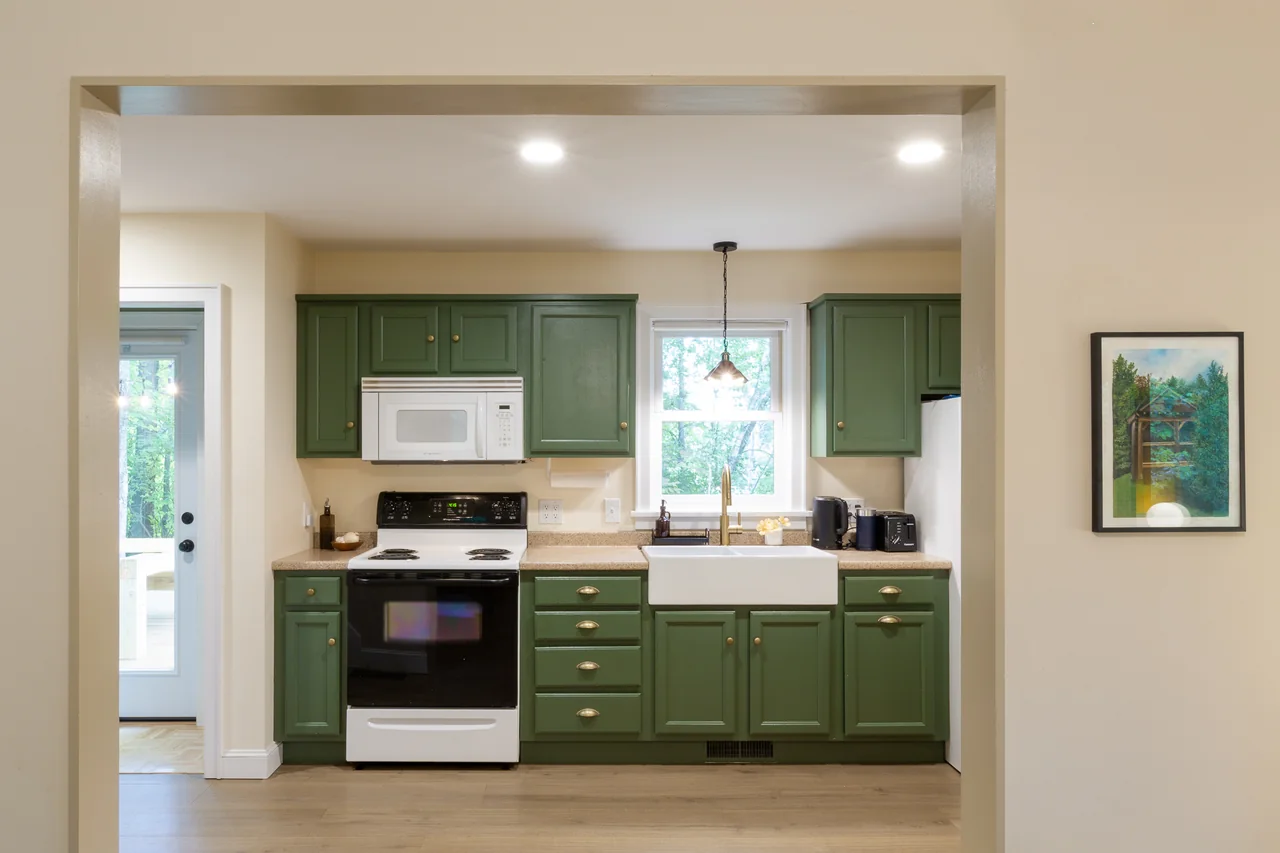 Green kitchen cabinets beneath two windows